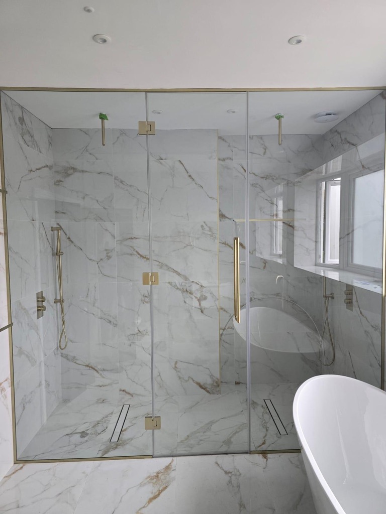 Frameless glass shower enclosure with brass hinges against marble