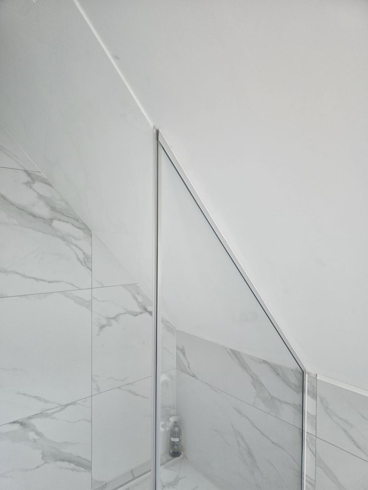 Glass shower screen with chamfered top edge to follow a sloped ceiling